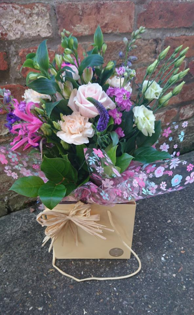 Happiness - Lovely fresh flowers in water presented in a gift bag. Nix mix of seasonal flowers in pale pinks, purples, white to include greenery.